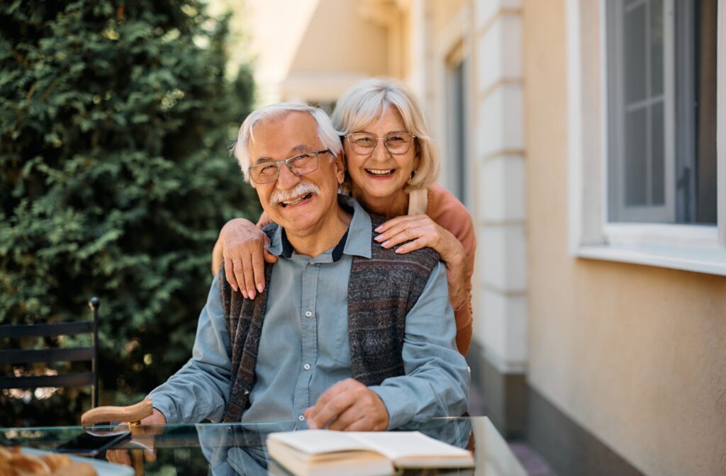 A senior couple stands together happily outsider of their new senior living facility.