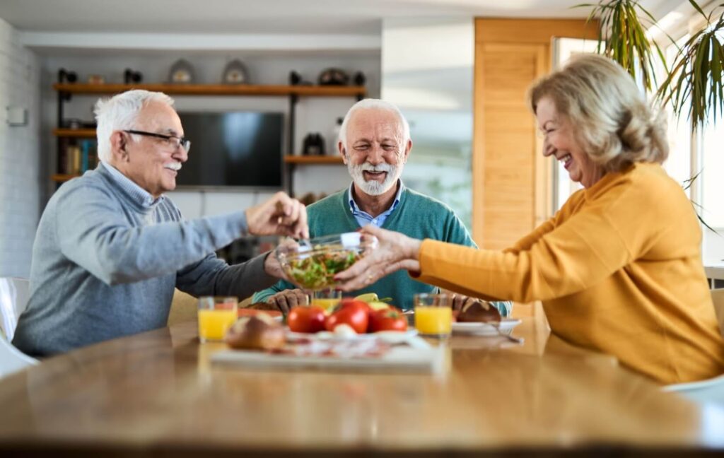 A group of older adults share a healthy meal together in their senior living community's shared dining room.