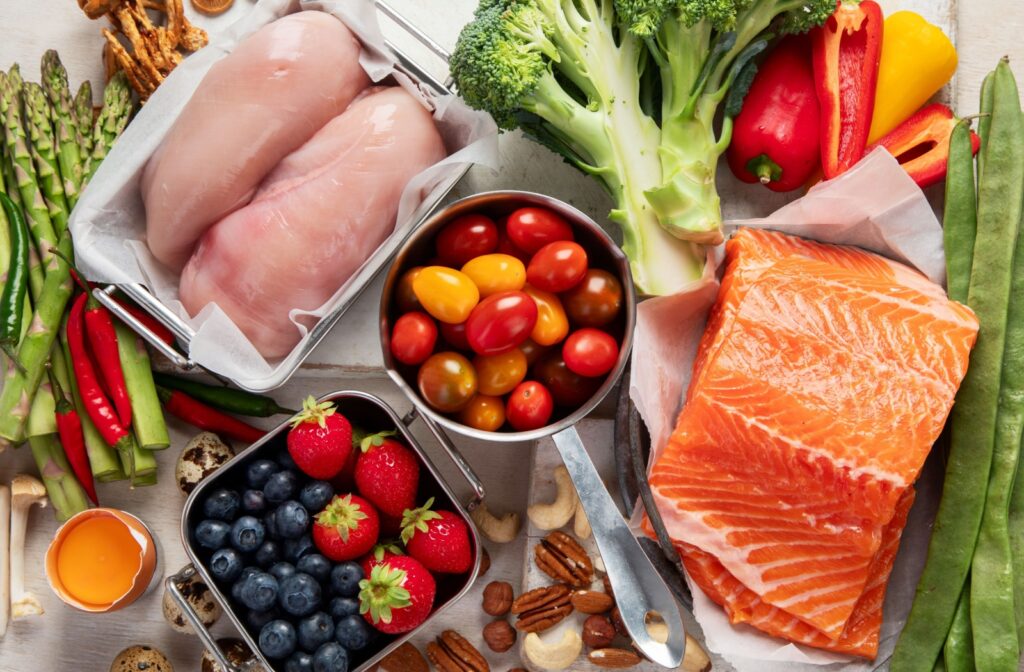 A pile of keto-friendly foods including salmon, chicken, nuts, and tomatoes are placed artfully across a table.