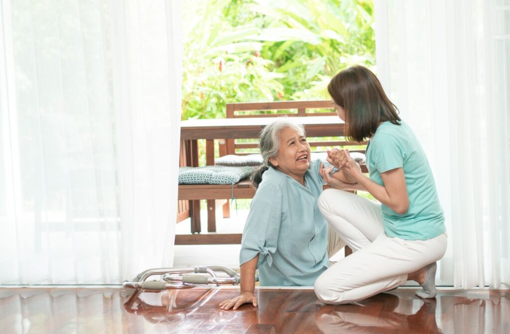 An adult carefully helps their older parent up off the floor after a fall trying to get outdoors
