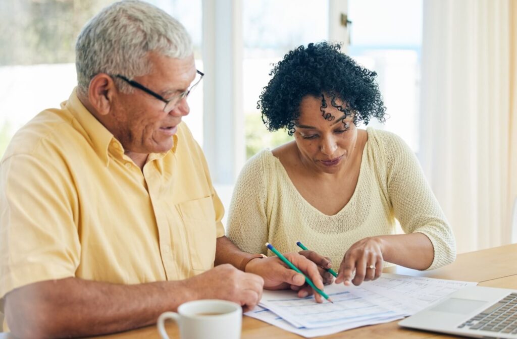 Two older adults fill out paperwork with pencils over coffee while planning for a future in senior living