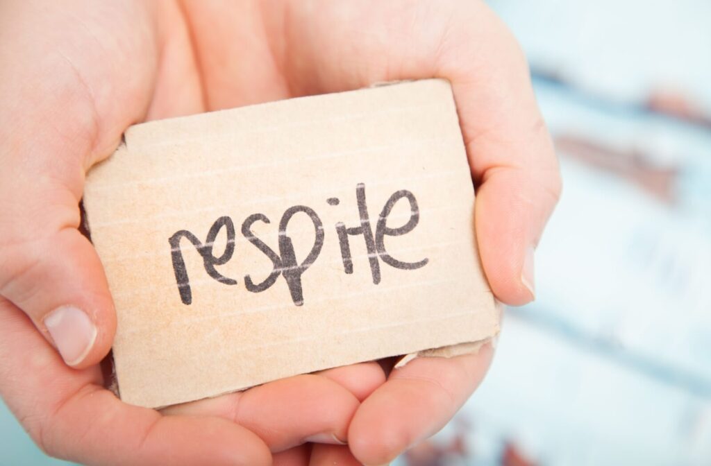 The word "respite" is written on a wooden block and being held by caring hands.