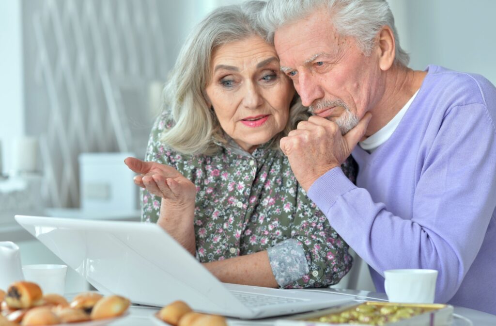 An older couple thoughtfully looks at a laptop on their table during a serious discussion about a potential move to senior living