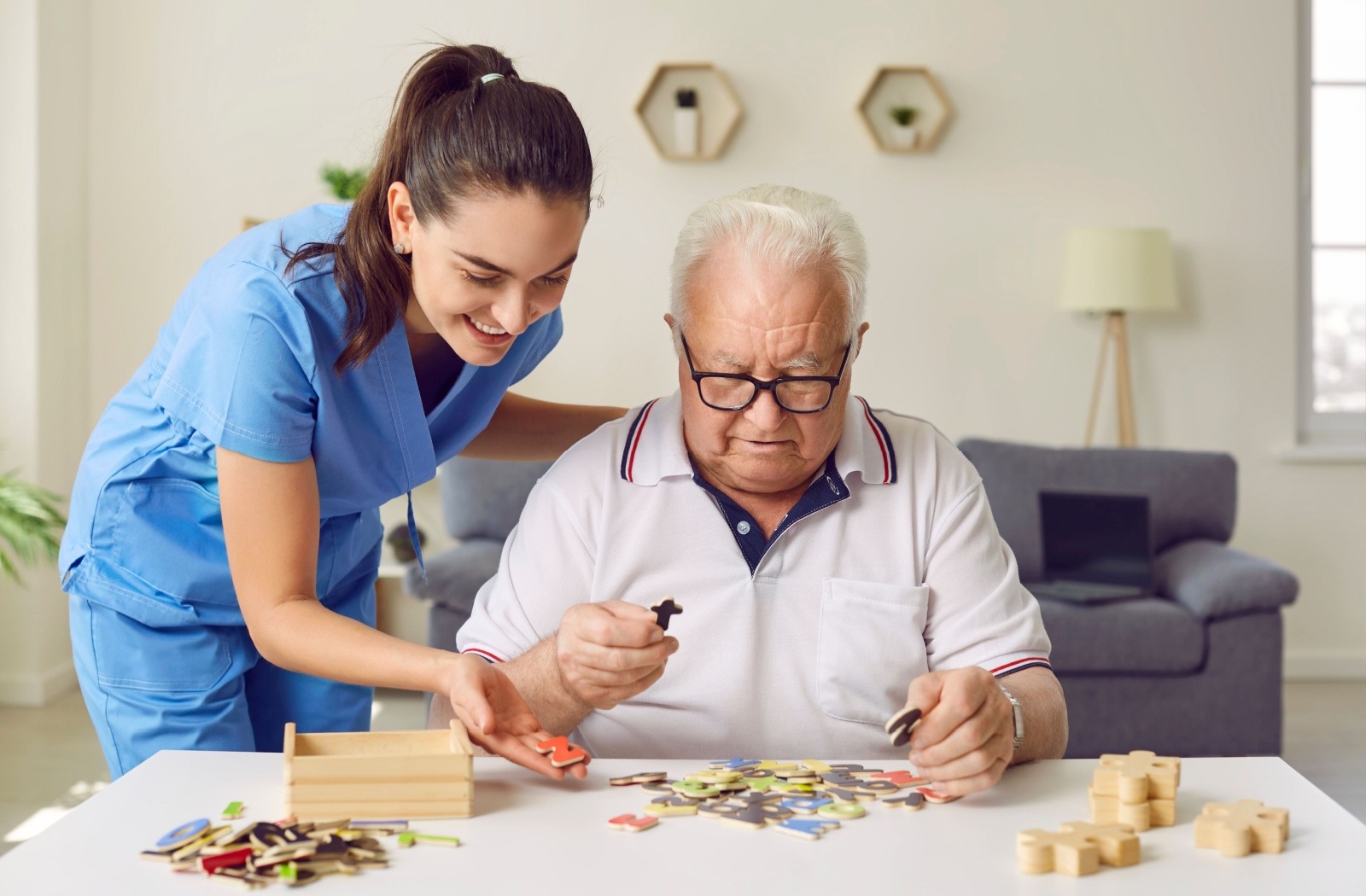 A caregiver helps a smiling senior put together a puzzle.
