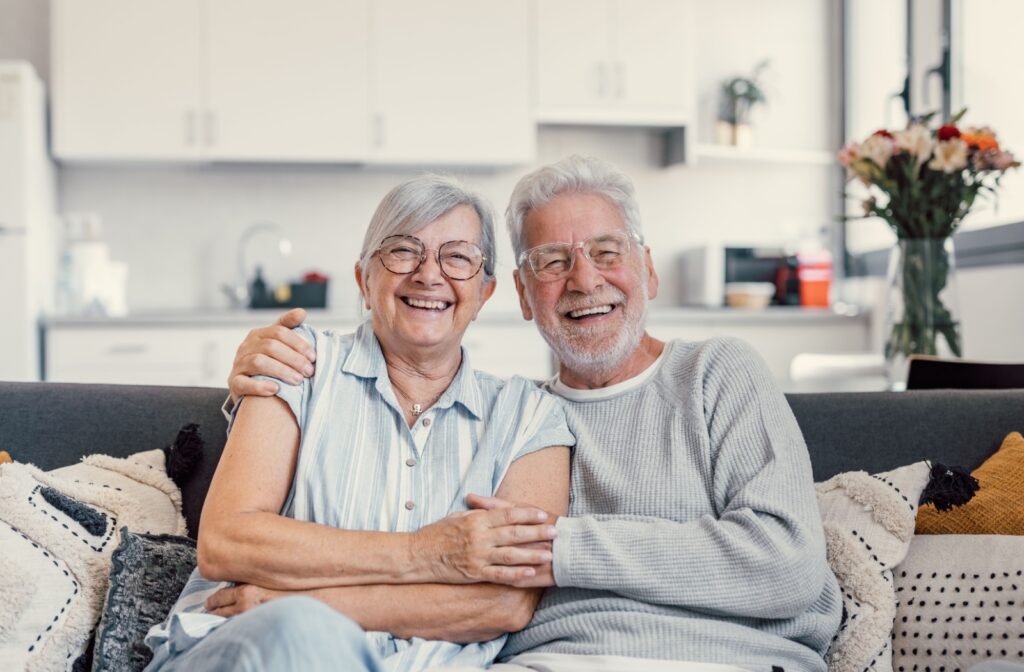 A senior couple smiles while sitting on the couch.
